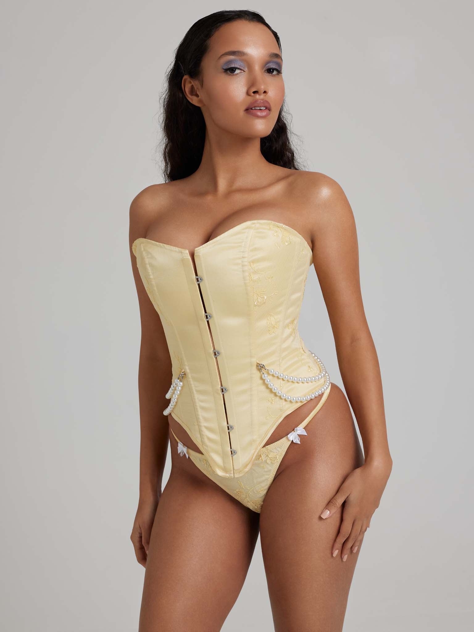 Woman wearing yellow corset with pearl detailing and busk closures and yellow thong with white bows