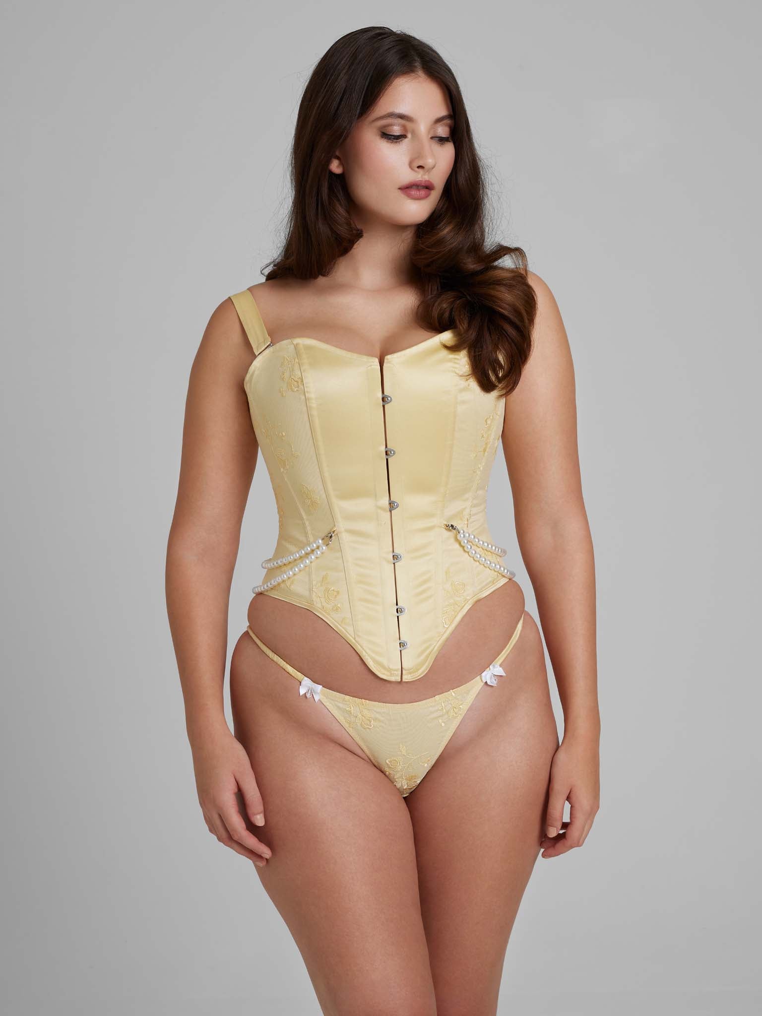 Woman wearing yellow corset with pearl detailing and busk closures and yellow thong with white bows